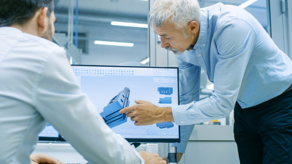 Three engineers in a modern lab discussing the design of a complex jet engine turbine assembly on a workbench.