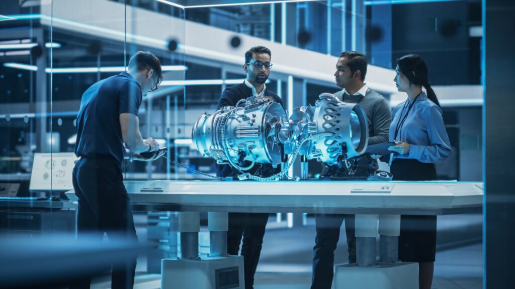 Senior engineer pointing at a 3D CAD model on a computer screen while discussing design details with a colleague.